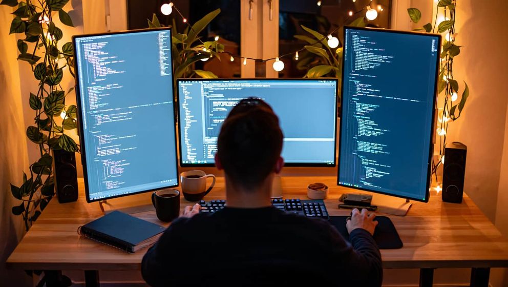 So funktioniert Vibe Coding Vibe Coder arbeitet bei Nacht an 3 Monitoren mit KI-Tools